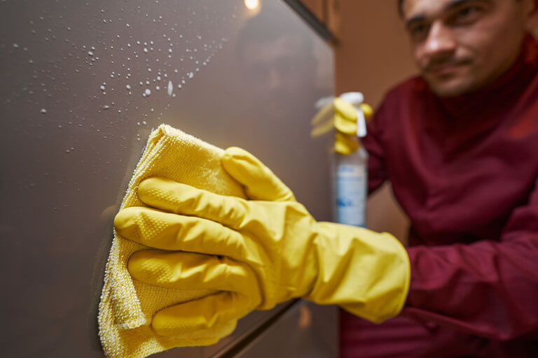 Cleaner wiping fridge with a smile